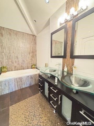 bathroom with tile patterned flooring, vanity, lofted ceiling, and tiled bath