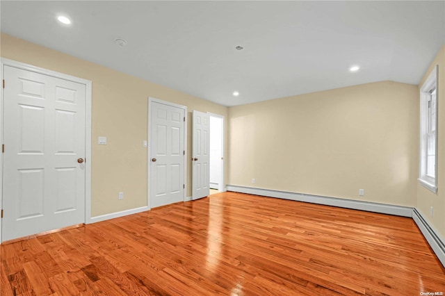 empty room featuring a baseboard heating unit, lofted ceiling, and light hardwood / wood-style flooring