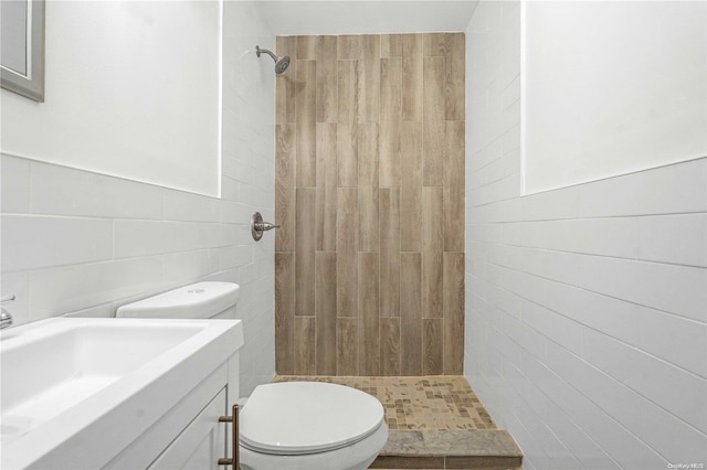 bathroom featuring tiled shower, toilet, tile walls, and sink