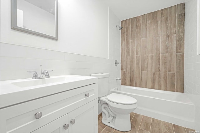 full bathroom with vanity, tiled shower / bath combo, wood-type flooring, tile walls, and toilet