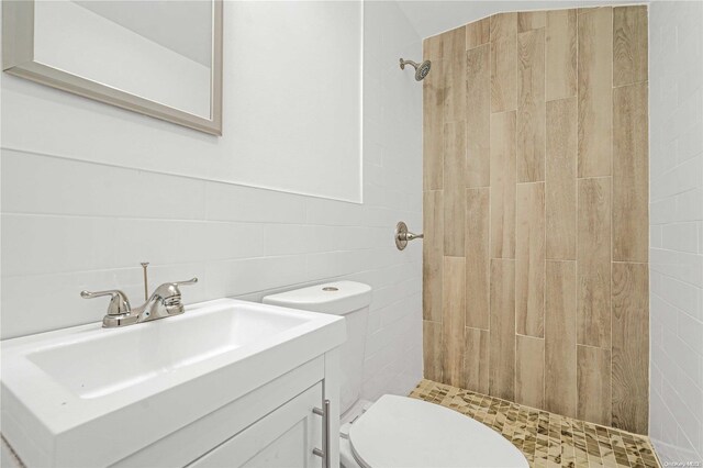 bathroom featuring a tile shower, vanity, tile walls, and toilet