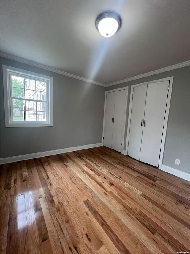 unfurnished bedroom featuring two closets, light hardwood / wood-style floors, and ornamental molding