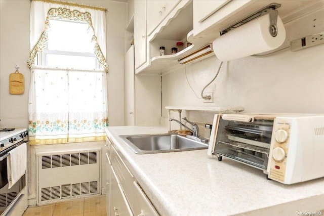 kitchen featuring white cabinets, stove, radiator, and sink