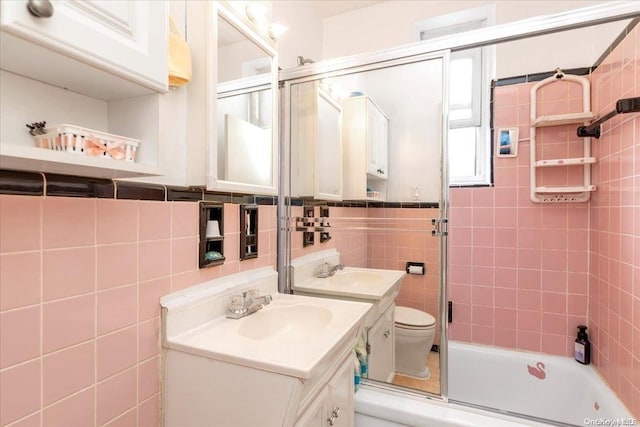 full bathroom featuring vanity, toilet, bath / shower combo with glass door, and tile walls