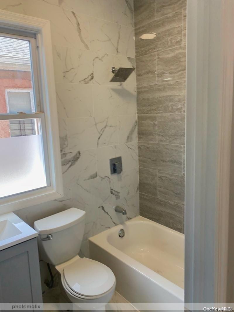 full bathroom featuring vanity, tiled shower / bath combo, and toilet