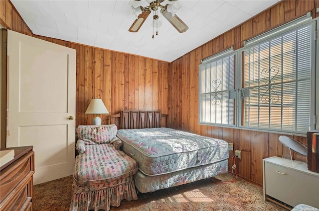 carpeted bedroom featuring ceiling fan and wood walls