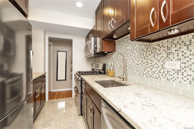 kitchen with dark brown cabinetry, sink, stainless steel appliances, tasteful backsplash, and light stone counters