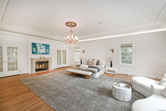 bedroom with french doors, an inviting chandelier, a high end fireplace, access to outside, and hardwood / wood-style flooring