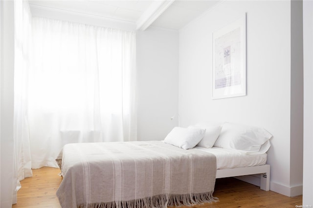 bedroom featuring beamed ceiling, light hardwood / wood-style floors, and ornamental molding