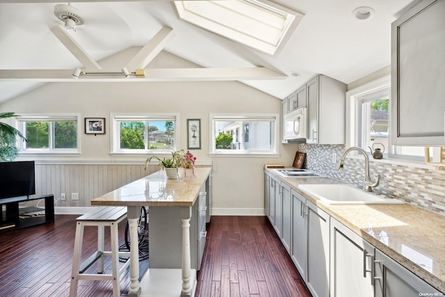 kitchen with gray cabinetry, lofted ceiling with skylight, sink, and dark wood-type flooring