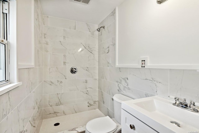 bathroom featuring toilet, vanity, tile walls, and tiled shower