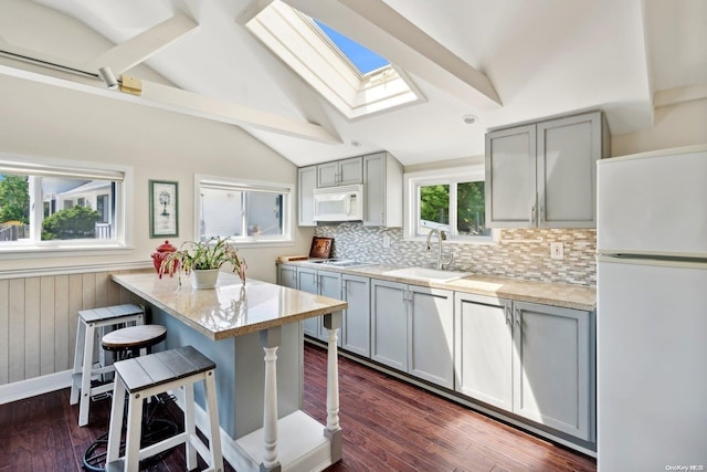 kitchen featuring white appliances, gray cabinets, a breakfast bar area, and sink