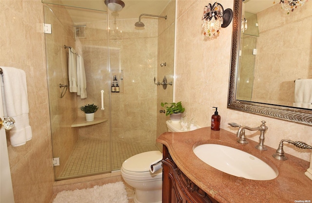 bathroom with vanity, toilet, tile walls, and a shower with shower door