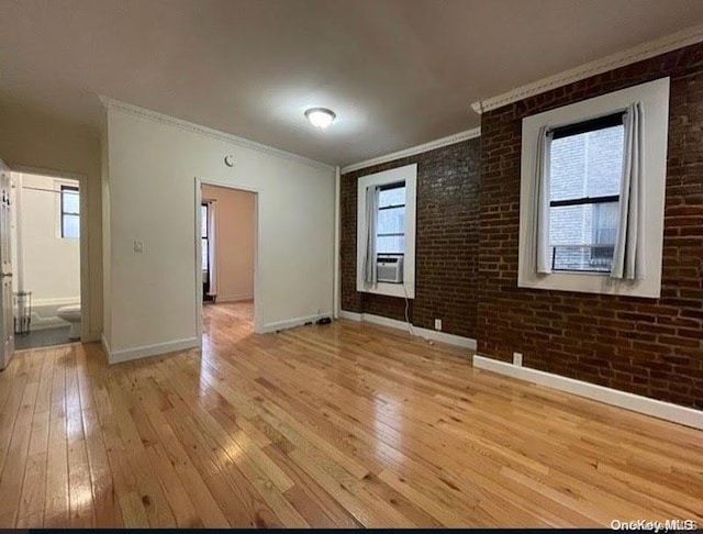 empty room with light hardwood / wood-style floors, cooling unit, ornamental molding, and brick wall