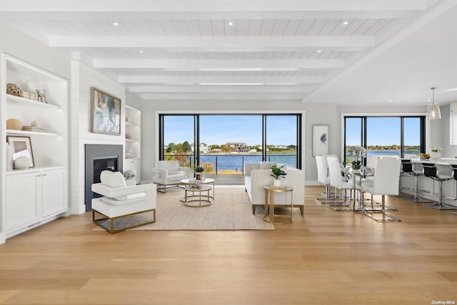 living room with beam ceiling, light wood-type flooring, a water view, and plenty of natural light