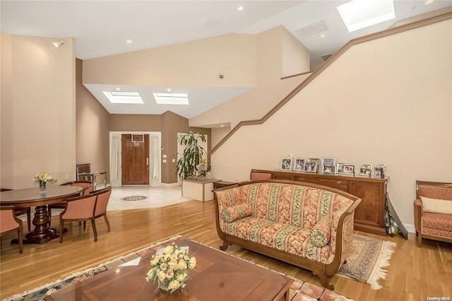 living room with a skylight, high vaulted ceiling, and light wood-type flooring