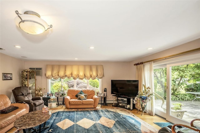 living room with a wall mounted air conditioner, a wealth of natural light, and light hardwood / wood-style flooring