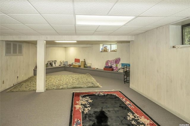 basement featuring carpet flooring, a drop ceiling, and wood walls