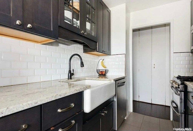 kitchen with sink, stainless steel appliances, light stone counters, backsplash, and tile patterned floors