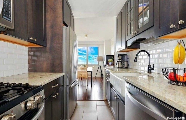 kitchen with light stone countertops, dark brown cabinets, stainless steel appliances, and dark tile patterned flooring