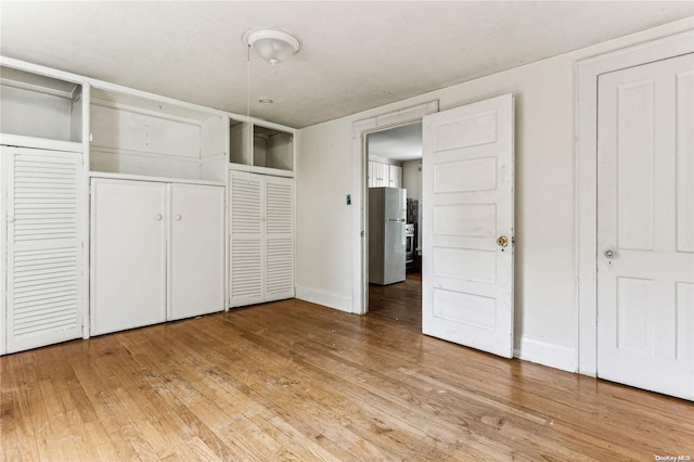 unfurnished bedroom with hardwood / wood-style floors, stainless steel refrigerator, and multiple closets