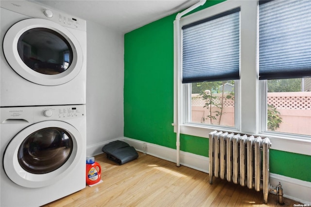 laundry area featuring stacked washer and dryer, radiator, and light hardwood / wood-style flooring