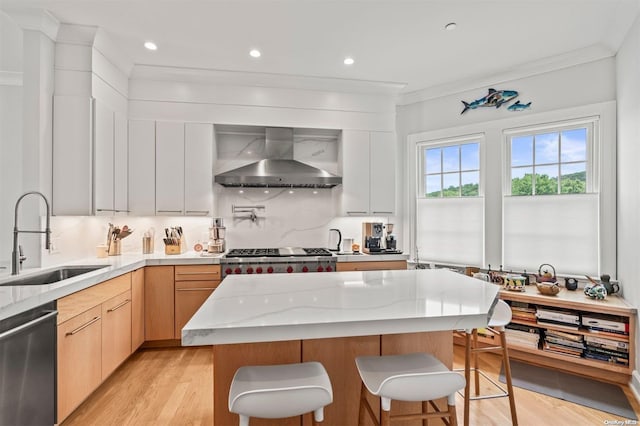 kitchen featuring sink, wall chimney range hood, light stone counters, light hardwood / wood-style flooring, and appliances with stainless steel finishes