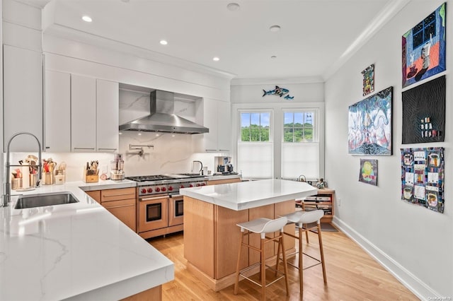 kitchen with range with two ovens, wall chimney exhaust hood, light wood-type flooring, a kitchen island, and white cabinetry