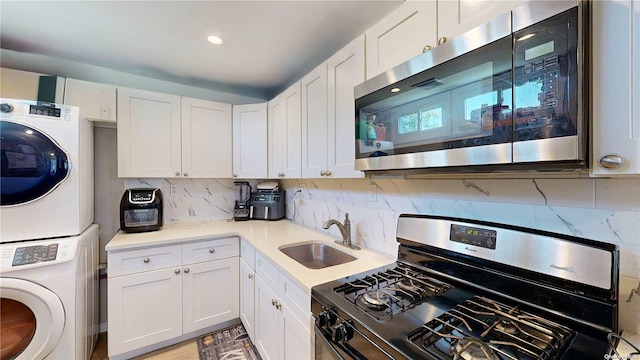 kitchen with sink, stainless steel appliances, decorative backsplash, white cabinets, and stacked washer and clothes dryer