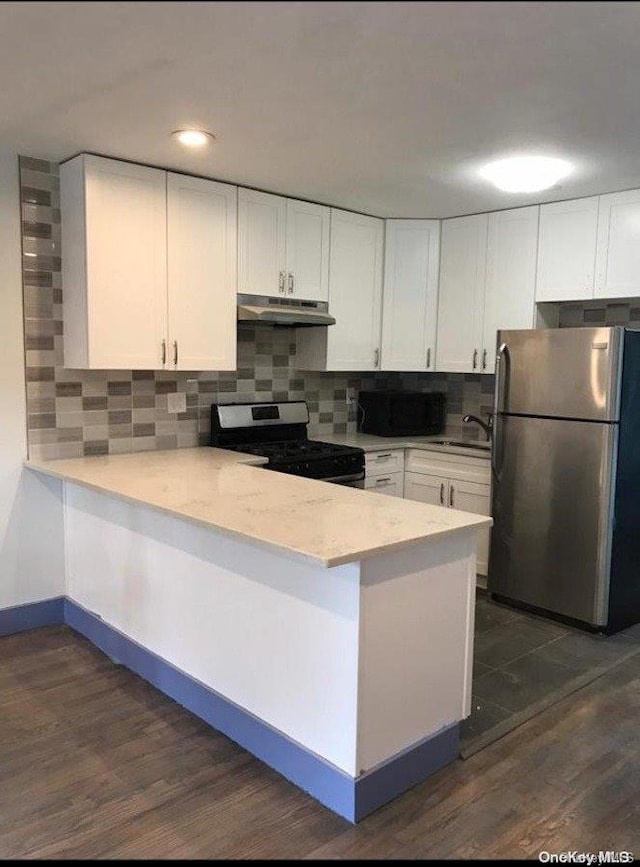 kitchen with kitchen peninsula, appliances with stainless steel finishes, dark hardwood / wood-style flooring, tasteful backsplash, and white cabinets