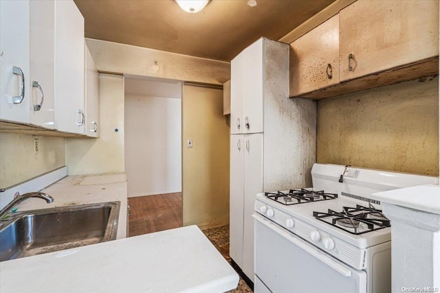 kitchen with white gas range oven, white cabinetry, dark wood-type flooring, and sink