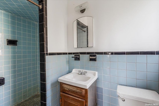 bathroom with tiled shower, vanity, toilet, and tile walls