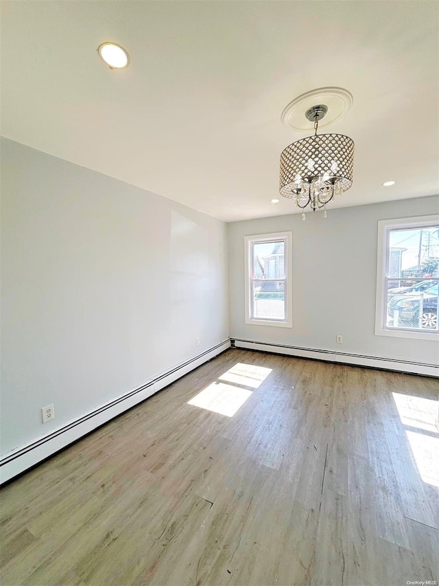 spare room featuring light hardwood / wood-style floors, baseboard heating, and an inviting chandelier