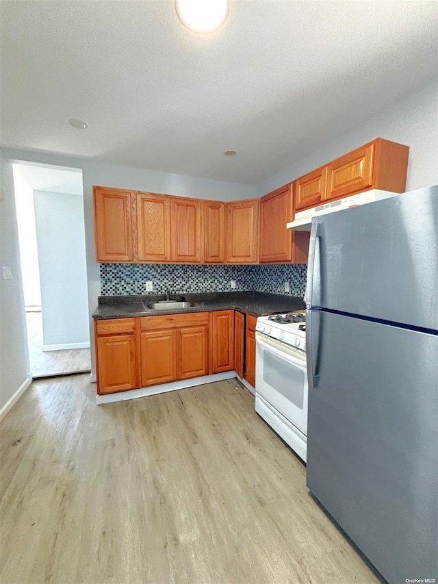 kitchen featuring white gas stove, sink, tasteful backsplash, stainless steel fridge, and light wood-type flooring