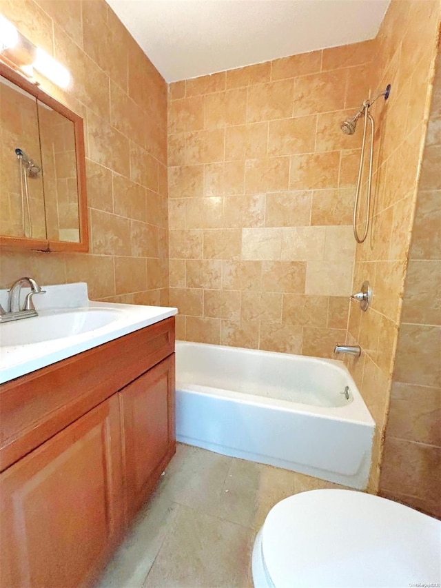 full bathroom featuring vanity, tiled shower / bath combo, toilet, and tile walls