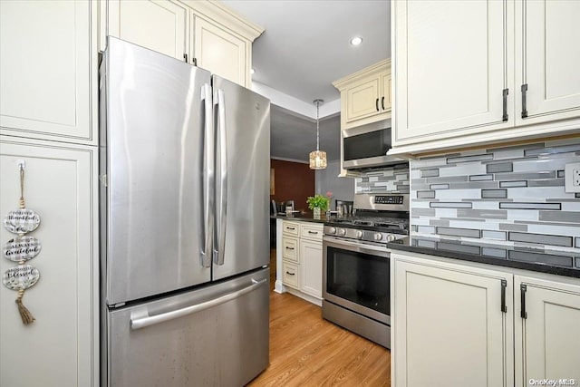 kitchen featuring stainless steel appliances, pendant lighting, cream cabinetry, decorative backsplash, and light wood-type flooring