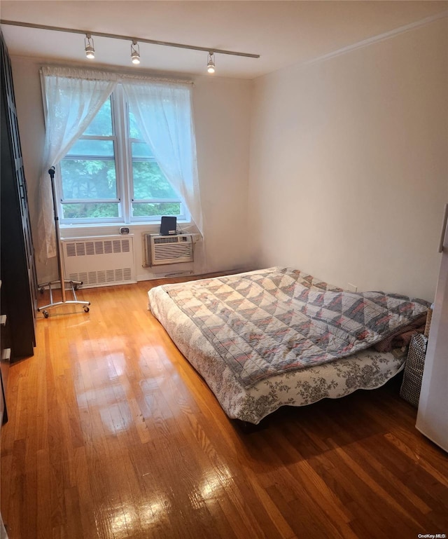 bedroom with radiator heating unit, hardwood / wood-style flooring, track lighting, and a wall unit AC