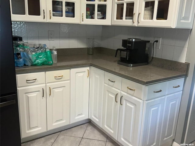 kitchen featuring backsplash, white cabinetry, black refrigerator, and light tile patterned floors