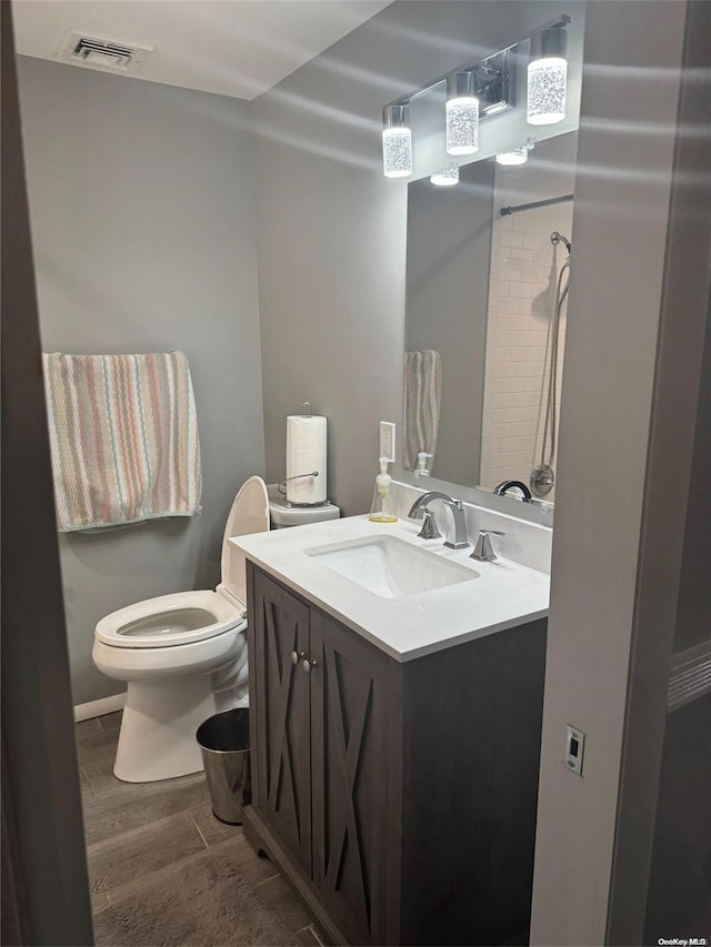 bathroom with tiled shower, hardwood / wood-style floors, vanity, and toilet