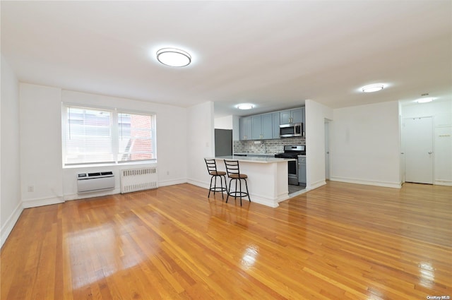 kitchen featuring tasteful backsplash, radiator, light countertops, appliances with stainless steel finishes, and a kitchen breakfast bar