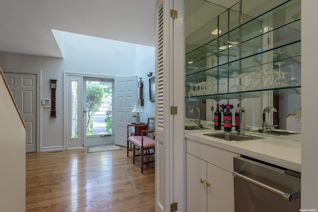 bar with stainless steel dishwasher, white cabinetry, light wood-type flooring, and sink