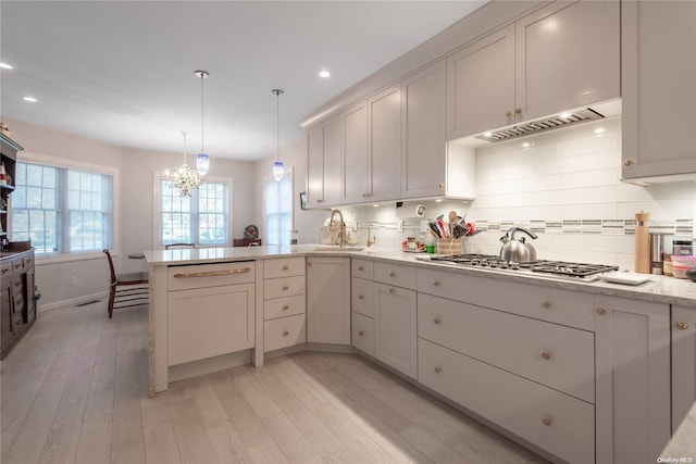 kitchen with kitchen peninsula, decorative backsplash, light wood-type flooring, stainless steel gas cooktop, and pendant lighting