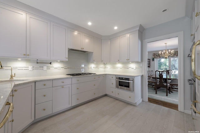 kitchen with light wood-type flooring, tasteful backsplash, stainless steel appliances, sink, and a notable chandelier