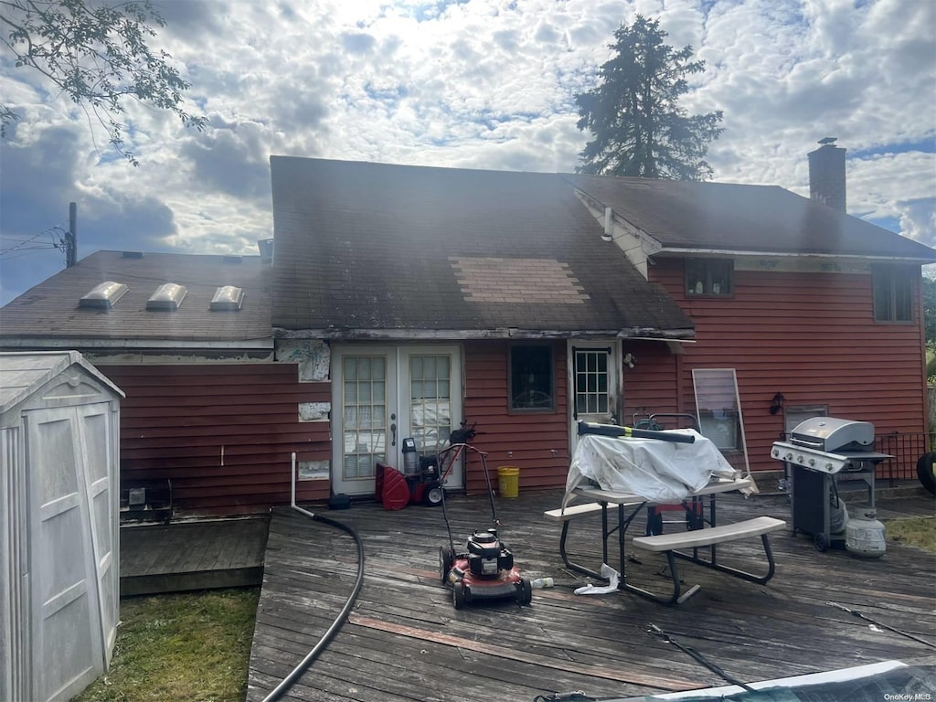 back of property with a wooden deck, french doors, and a storage shed