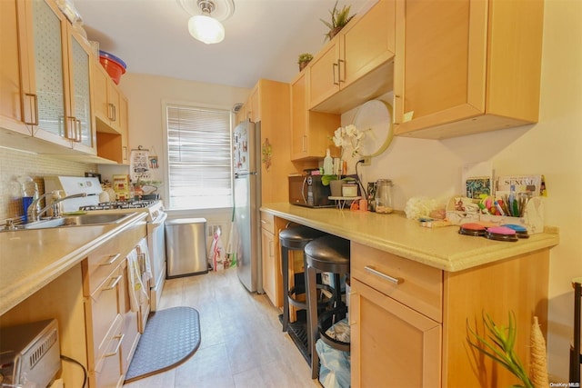 kitchen featuring light brown cabinetry, white gas range oven, stainless steel refrigerator, and sink