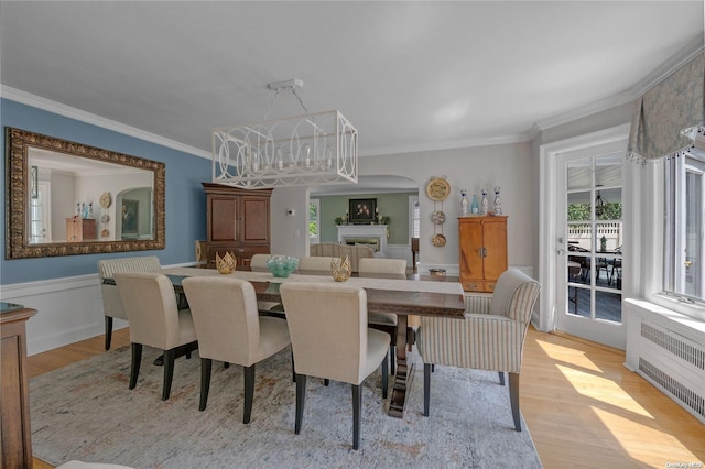 dining area featuring radiator heating unit, ornamental molding, and light wood-type flooring