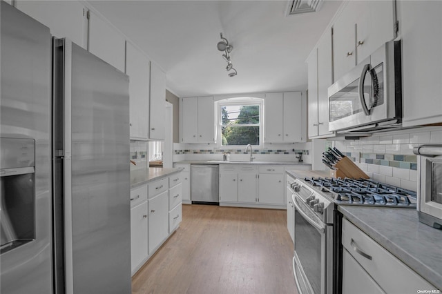 kitchen featuring decorative backsplash, stainless steel appliances, sink, white cabinets, and light hardwood / wood-style floors