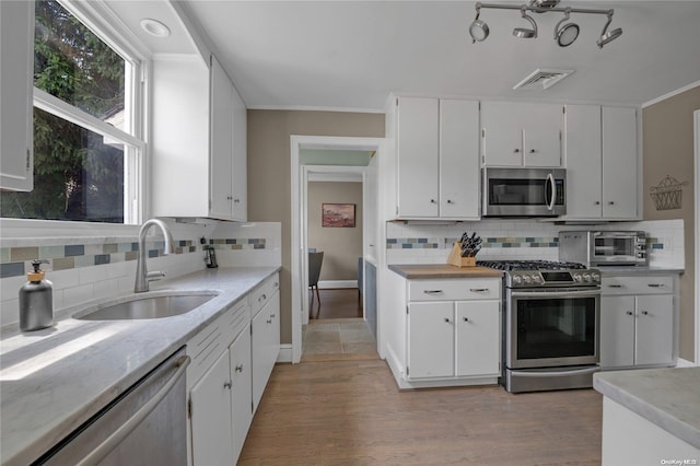 kitchen featuring white cabinets, backsplash, appliances with stainless steel finishes, and light hardwood / wood-style flooring