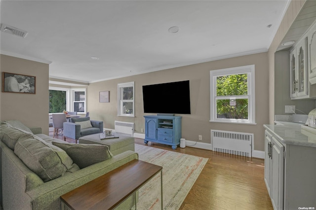 living room with radiator heating unit, ornamental molding, and light hardwood / wood-style flooring