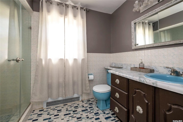 bathroom featuring tile patterned floors, toilet, a shower with door, vanity, and tile walls